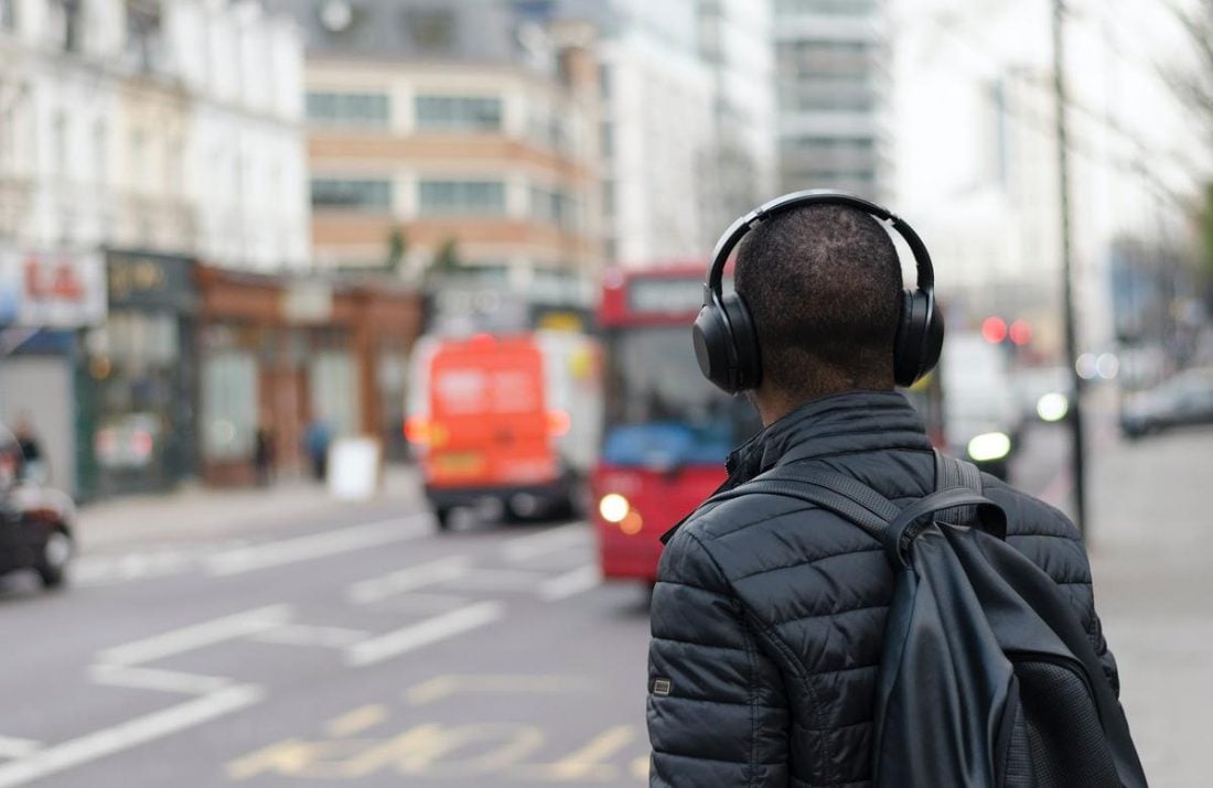 Man wearing headphones on a city sidewalk (From:Unsplash).