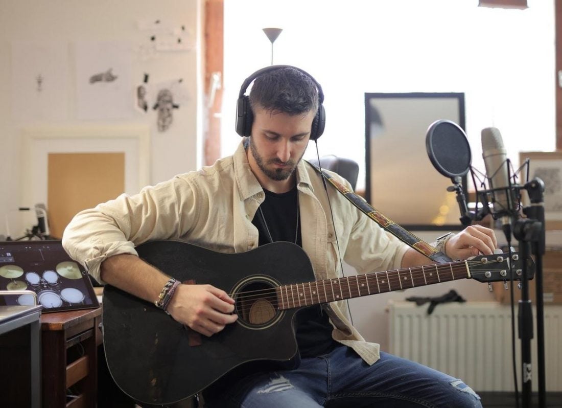 A man plays the guitar with his headphones on (From Pexels.com)