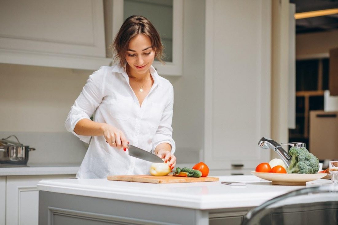 Woman wearing white shirt chopping ingredients at home while smiling (From: Pxhere.com)