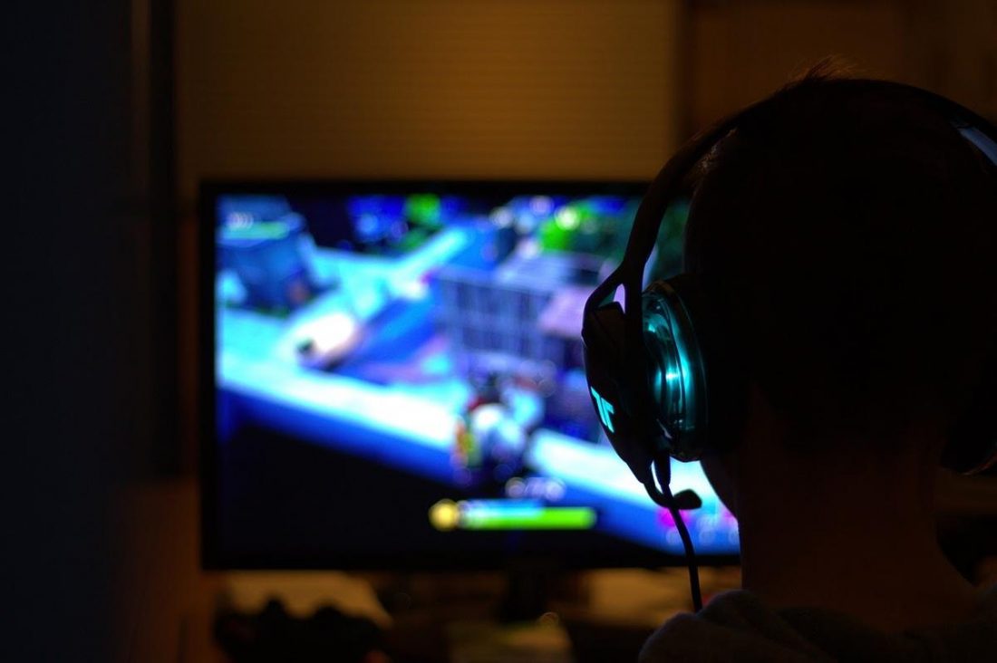 Gamer listening to music with headphones while playing fortnight in a dark room (From: Pixabay.com)